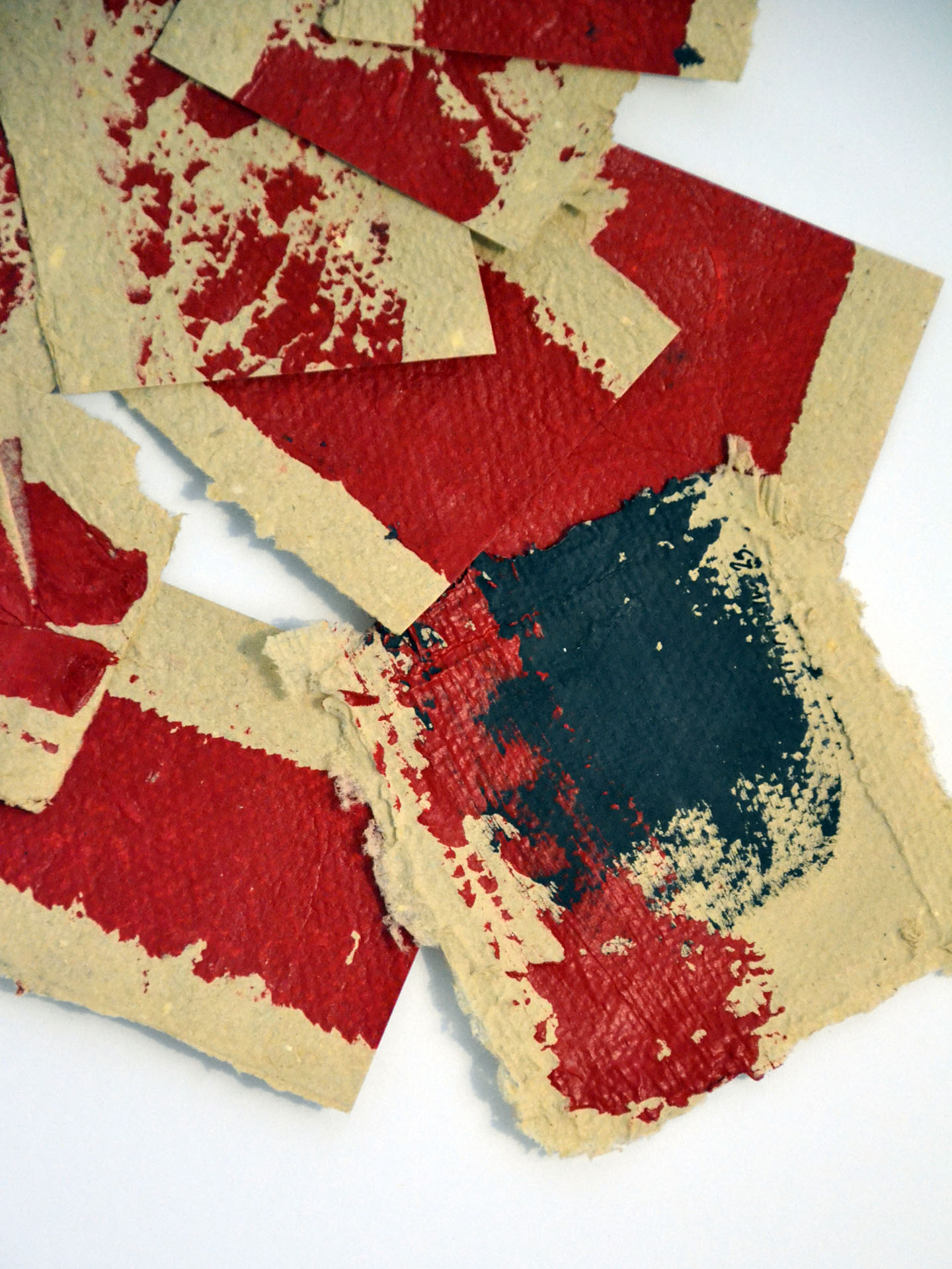 Primer plano de la obra "Deconstruyendo II" que muestra la superposición de fragmentos de papel artesanal. Detalle de la mancha de pintura roja vibrante y el contraste con el papel ocre texturizado y la pincelada negra matérica en La Oculta Gallery.