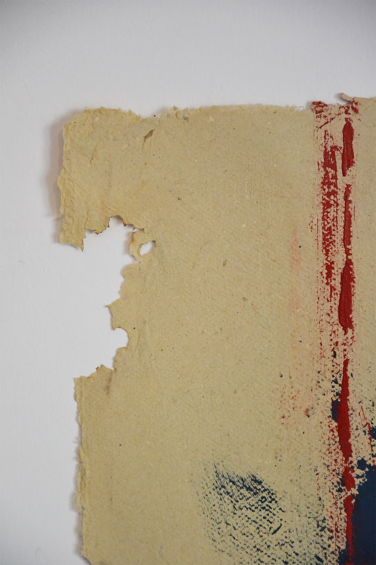 Primer plano del borde orgánico y desgarrado de la obra "Desdibujando el límite". Se aprecia la textura del papel grueso y el relieve de la pintura roja matérica sobre el soporte ocre.